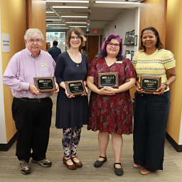 Four Rails board member stand side-by-side, each holding a plaque in front of the Deirdre Brennan Meeting Room doors.