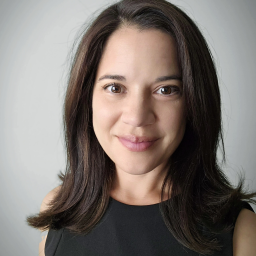 A headshot of Maggie Thomann against a gray background.