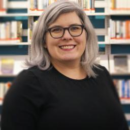 Susan Conner smiling, posing in front of shelves in Library