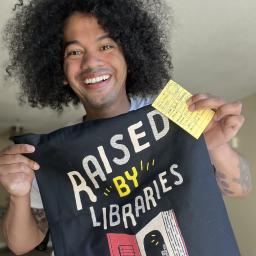 Mychal Threets holds up a T-shirt that says "Raised by Libraries"