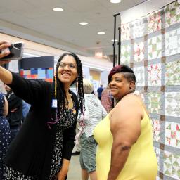 Palatine Public Library Workshop Manager Selicia Applegate and Palatine resident Tiffany Wilhoite stand in front of exhibit's Freedom Quilt. They are smiling as they take a selfie.