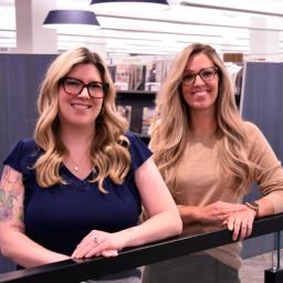 (left) Amy Prochot, Deputy Director of Operations, (right) Stephanie Driscoll, Deputy Director of Public Services are standing together in library setting.