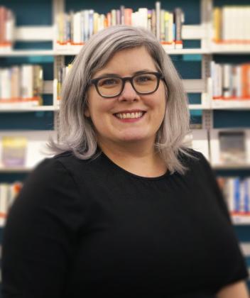 Susan Conner smiling, posing in front of shelves in Library