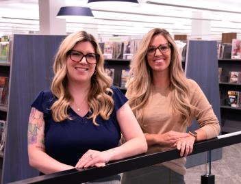 (left) Amy Prochot, Deputy Director of Operations, (right) Stephanie Driscoll, Deputy Director of Public Services are standing together in library setting.