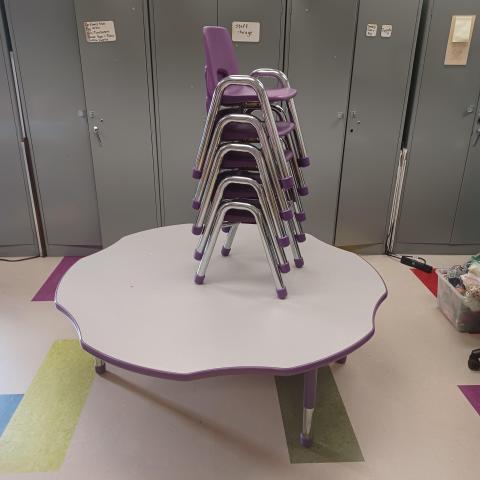 Image of semi-round table with five small purple and metal chairs stacked on it