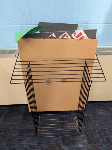 A black wire-framed poster board rack, with a cardboard inserted in the back slot.