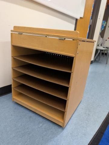 A cube-shaped wooden storage unit with 5 shelves on one side, typically used for storing big books.