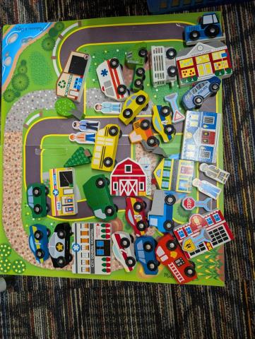 A set of wooden vehicles, including police, ambulance, and cars, all resting on a plastic road map.