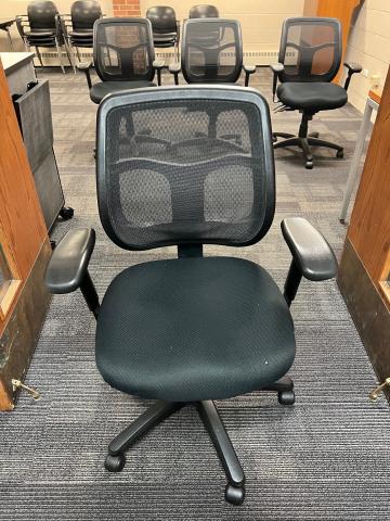Black mesh office desk chair in foreground with three additional black mesh chairs in background