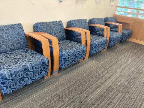 4 blue chairs with wooden arms, in a row against a cream wall, on grey carpeting