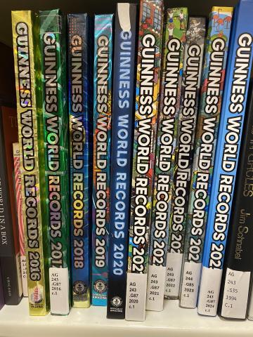 Nine editions of Guinness World Records on a library shelf.