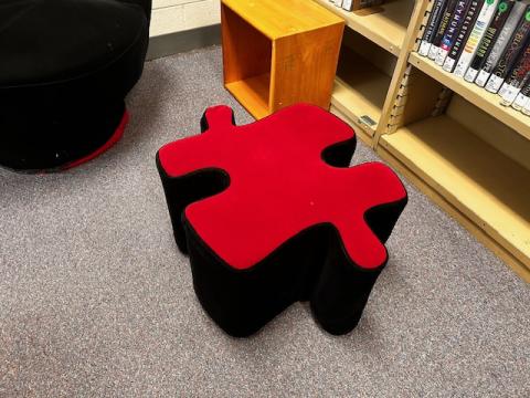 Footstool shaped like a puzzle piece, red on top and black on the sides, approximately 12 inches high and 18 inches long