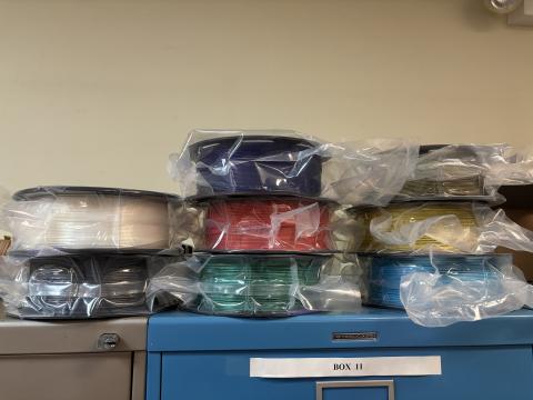 Pile of 8 unopened filament spools on top of a cabinet