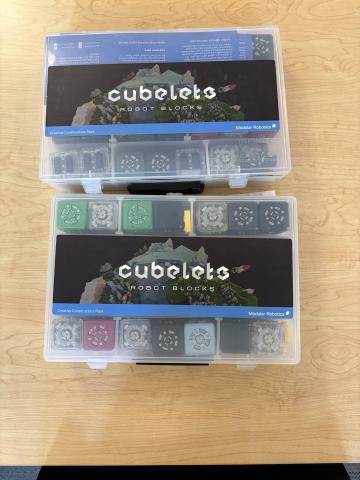 two clear boxes full of Cubelets on a light wooden table