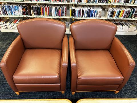 a pair of red-brown vinyl upholstered arm chairs in a library