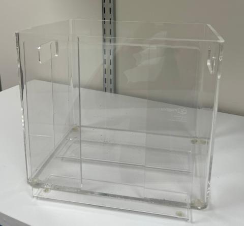Clear acrylic newspaper storage box on white shelf.