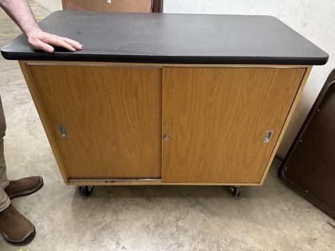 Wooden AV cabinet on wheels, has solid black top. 