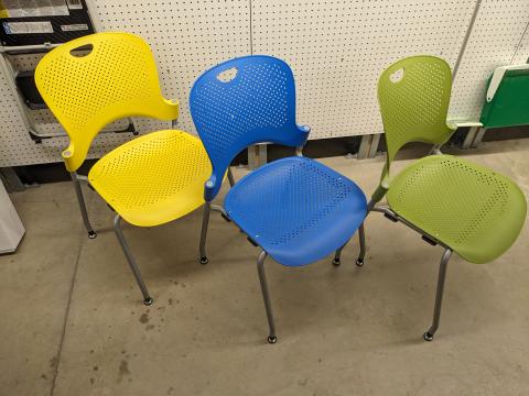 Three caper chairs adult size side by side, one yellow, one blue, one green.