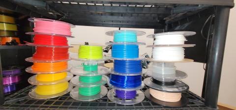 Spools of filament in shades of pink, red, orange, yellow, green, blue, white, translucent, black, and neutral