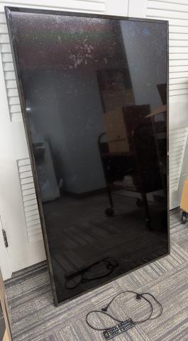 The TV lying on one of it's short sides against a closet, with the power cord and remote in the foreground.