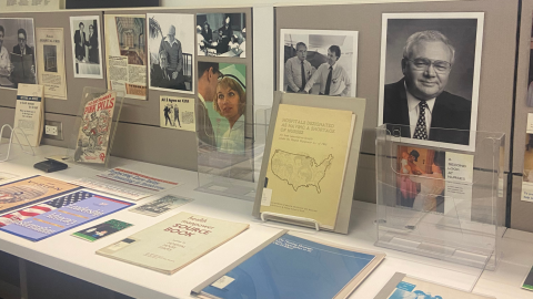 A display of various hospital publications in easels and acrylic holders on a white table. Behind the table are beige bulletin boards showing pictures of people in medical settings.