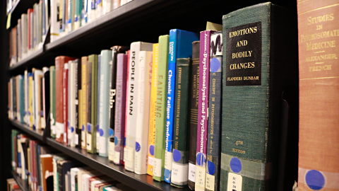 A bookshelf full of titles about psychology, the one in the forefront titled “Emotions and Bodily Changes” by Flanders Dunbar. 