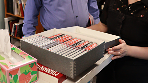 Two staff members hold open an archival box filled with cassette tapes. 