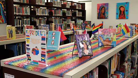 A pride month book display decorated with a sequined rainbow tablecloth.  