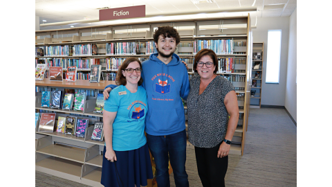 Three Fox River Grove Memorial Library employees stand next to each other in front of a bookshelf.