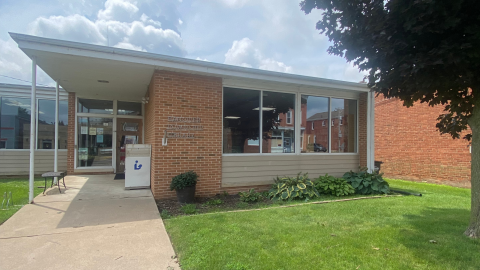 The main entrance of the Hanover Township Library, a one-story red brick building with windows, glass doors, and some beige siding.