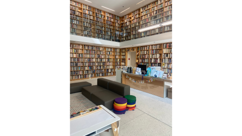A seating area with a sofa and a circulation desk situated in the corner of a library before two-story shelves full of books. 