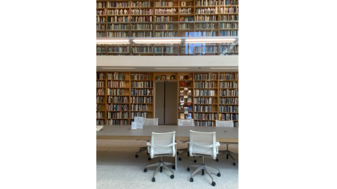 White chairs around a table in front of two-story library shelves