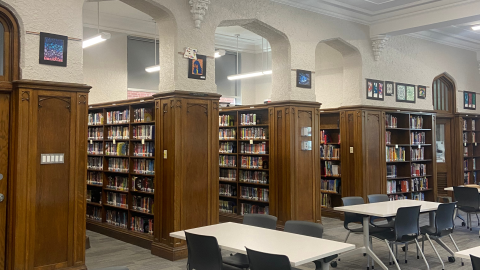 White tables with gray chairs in front of archways leading into aisles of bookshelves.