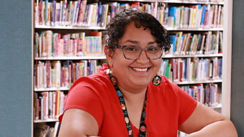 Diana Wence leans on a wall frame with books in the background.