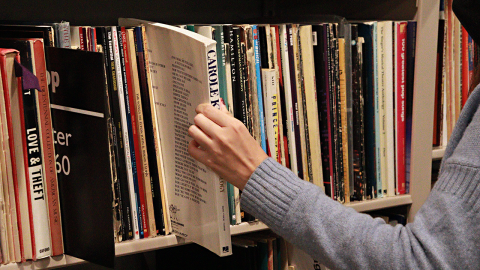 A hand pulls out a book from a bookshelf. 