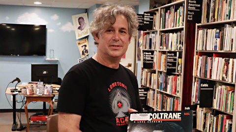 Colby Maddox stands in a room filled with books, holding up a Coltrane album. 