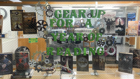 A steampunk themed window display in the library showcases a number of steampunk books and the caption, "Gear up for a year of reading." 