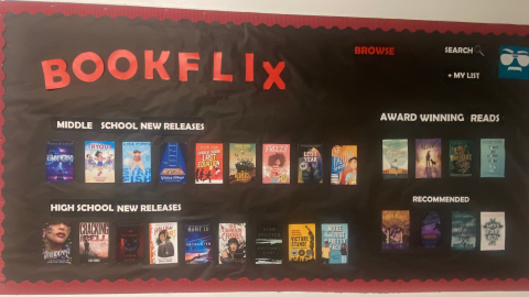 A bulletin board display decorated to resemble the Netflix streaming platform. The bulletin board is covered in black paper with a red border and features book covers arranged by audience. The board reads, "Bookflix. Browse, Search, My List. Middle School New Releases. Award Winning Reads. High School New Releases. Recommended."