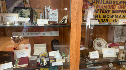 A glass-front display case holding shelves of memorabilia and artifacts from Oneida Historical Museum. 