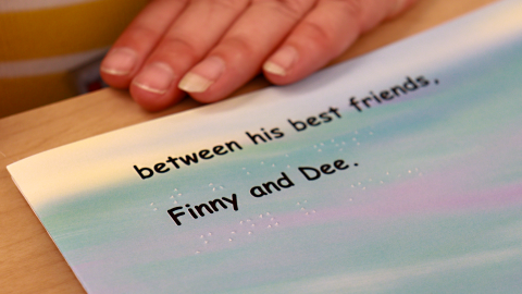 A page from a book that reads “between his best friends, Finny and Dee” in text and braille.  