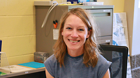 Ellen Shrader sits behind a desk and smiles at the camera. 