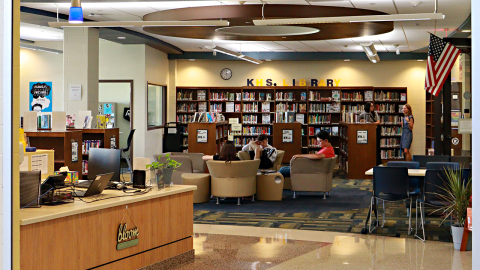 A school library with students sitting in chairs in front of a wall-to-wall bookshelf in the background. 