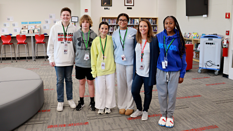 School librarian Heather McCarthy stands with five students in the center of the library. 