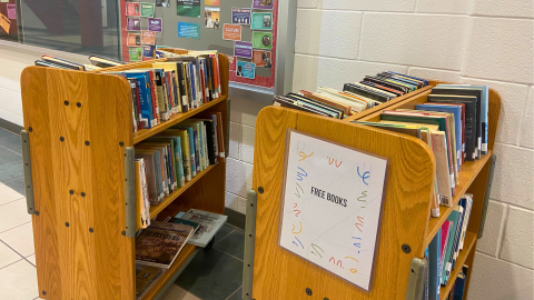 Two double-sided wooden book carts hold library books that are free for students. A sign on the cart on the right reads, "Free Books."