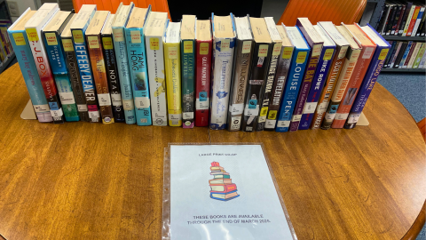 A display of various large print library books sitting on a wooden table with a paper sign reading, "Large Print Co-op. These books are available throug the end of March 2025."