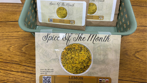 Spice of the Month card with QR code for information about lemon pepper. A basket holds packets of lemon pepper for 