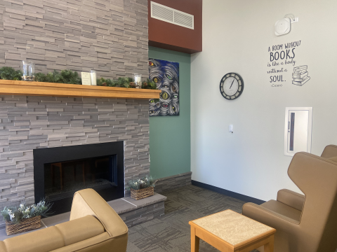 A fireside seating area features two comfy, wingback chairs and tables. One wall features a quote in black that reads, "A room without books is like a body without a soul. - Cicero."