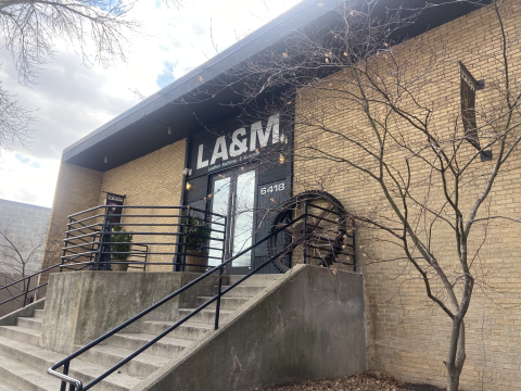 The front entrance to the Leather Archive & Museum, a tan brick building with black trim. A concrete staircase with black handrail leads to the glass double doors.