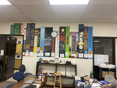 Large-format artwork showing various book spines from classic novels displayed on a light colored wall above a shelving unit. 