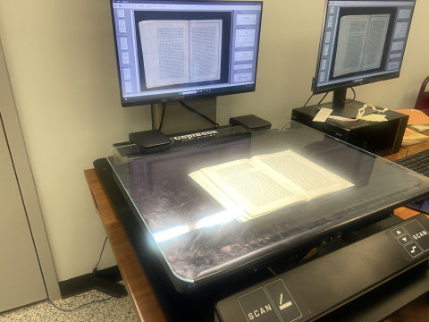 A CopiBook Open System book scanner is in use. The text below the plate is visible as is the scanned pages on the monitor screen.